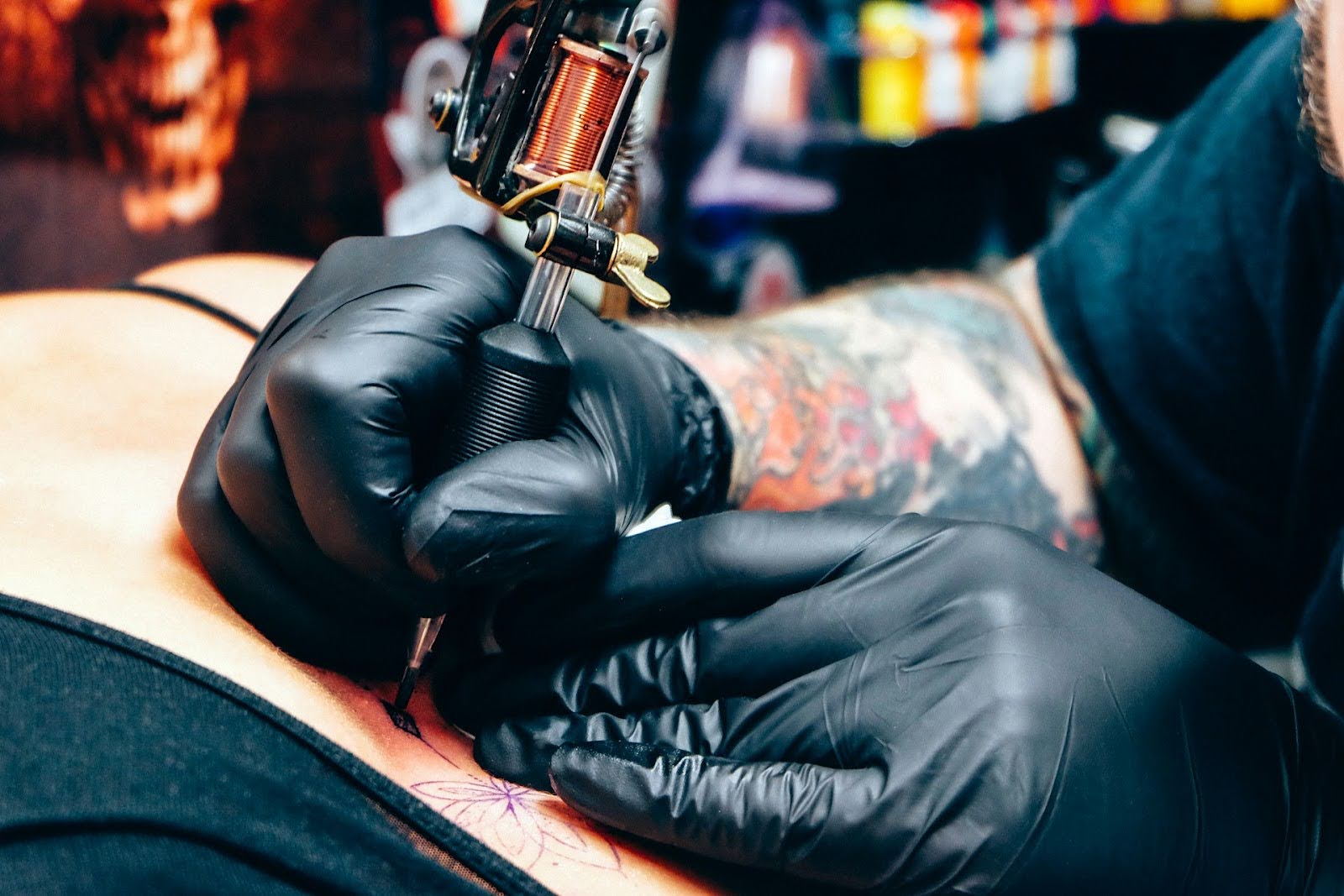 Tattoo artist wearing black gloves applying ink to skin with a tattoo machine in a studio setting