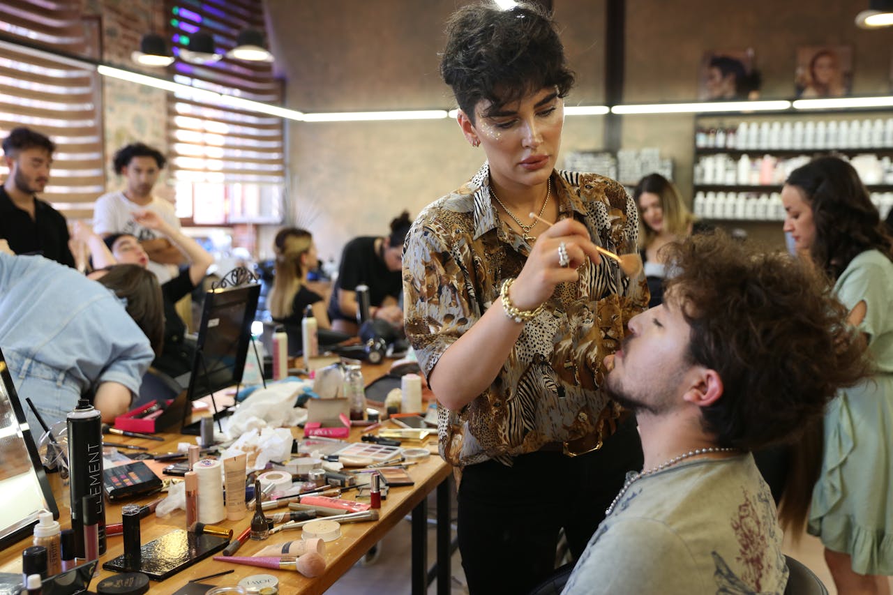 A MUA doing a model’s makeup in a crowded beauty studio