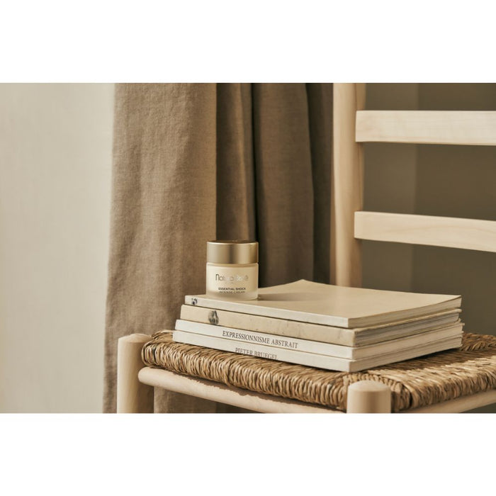 Natura Bisse Essential Shock Intense Cream stylized on top of a stack of books on a chair