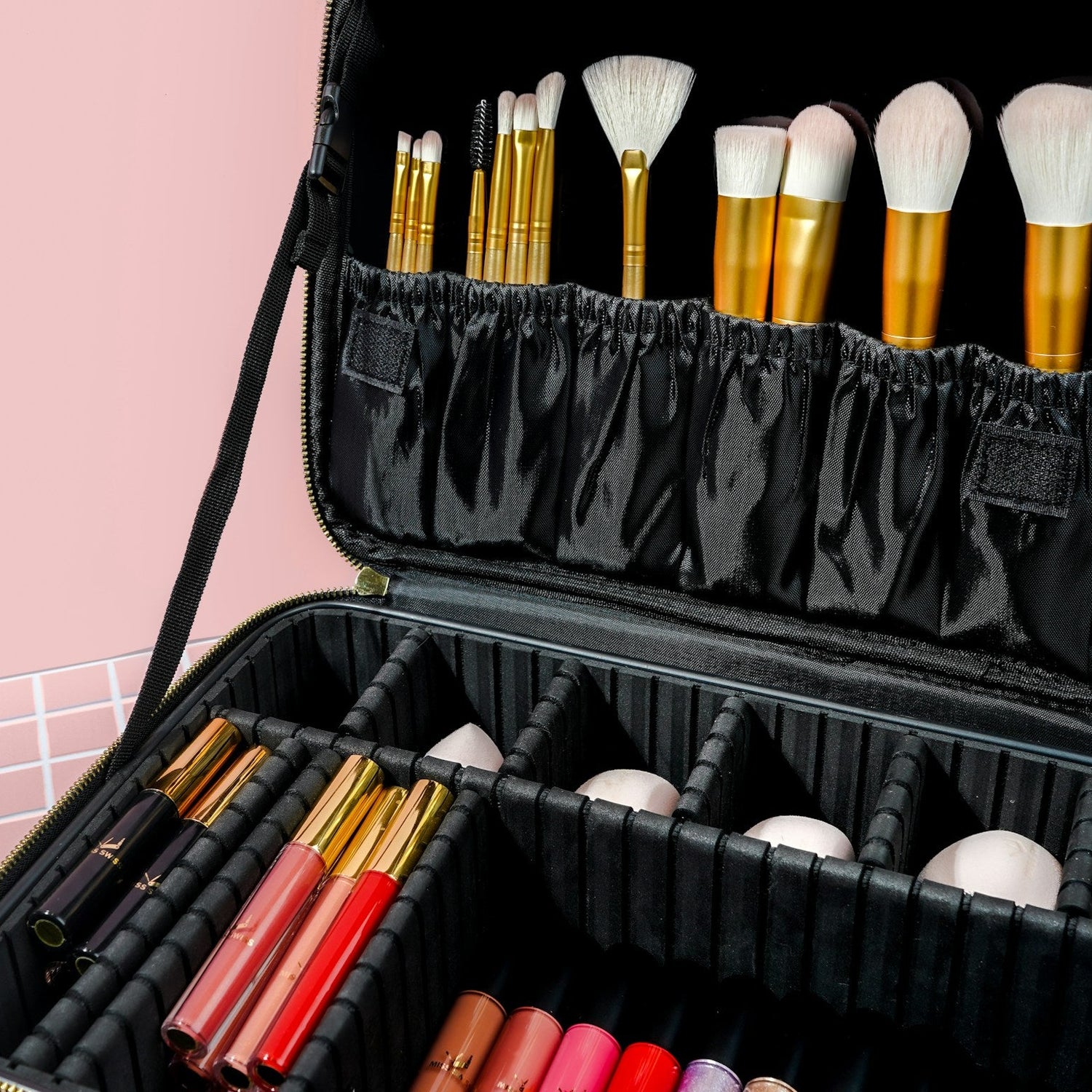 Black makeup kit with brushes against a pink background