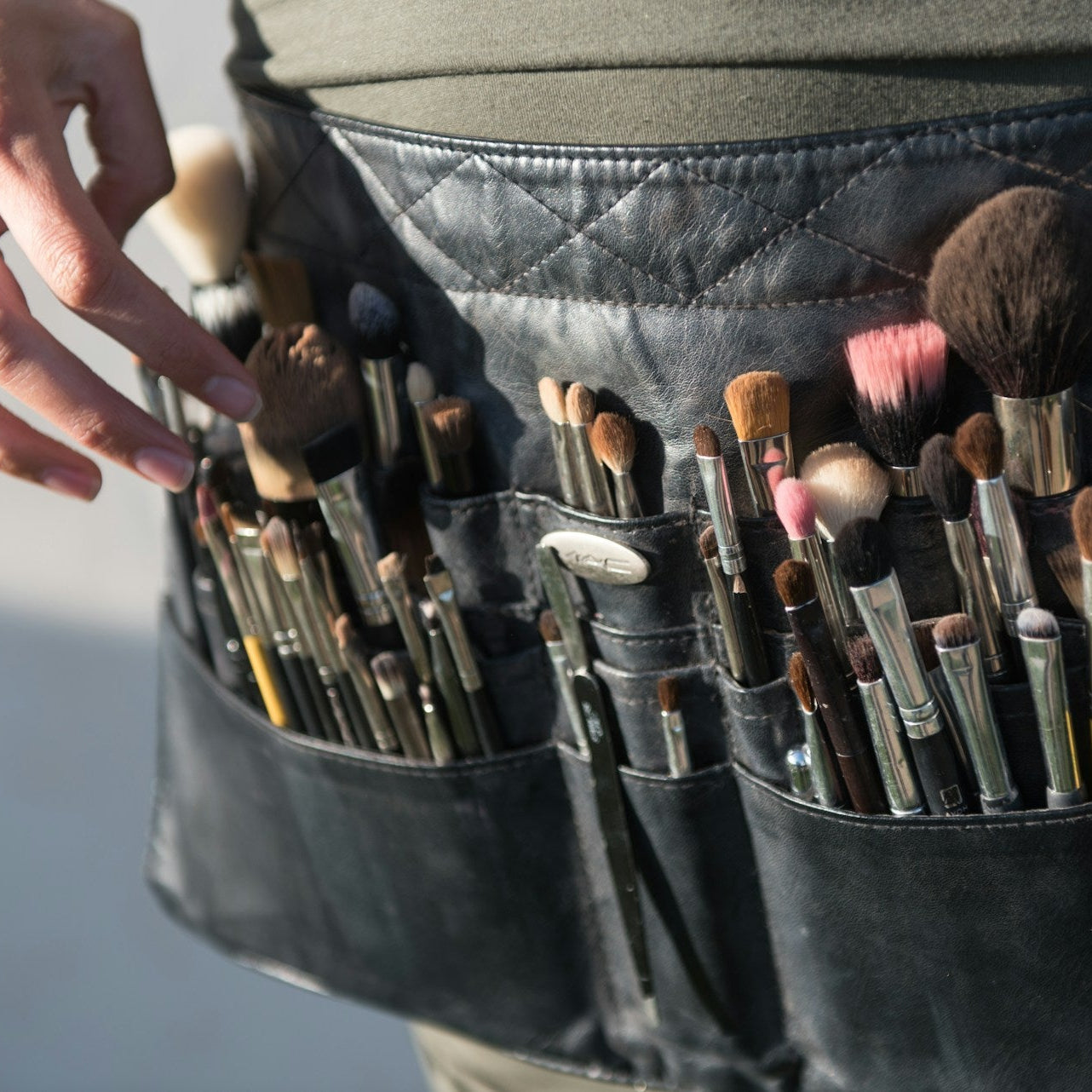 Close-up of a makeup tool belt with brushes around a person’s waist