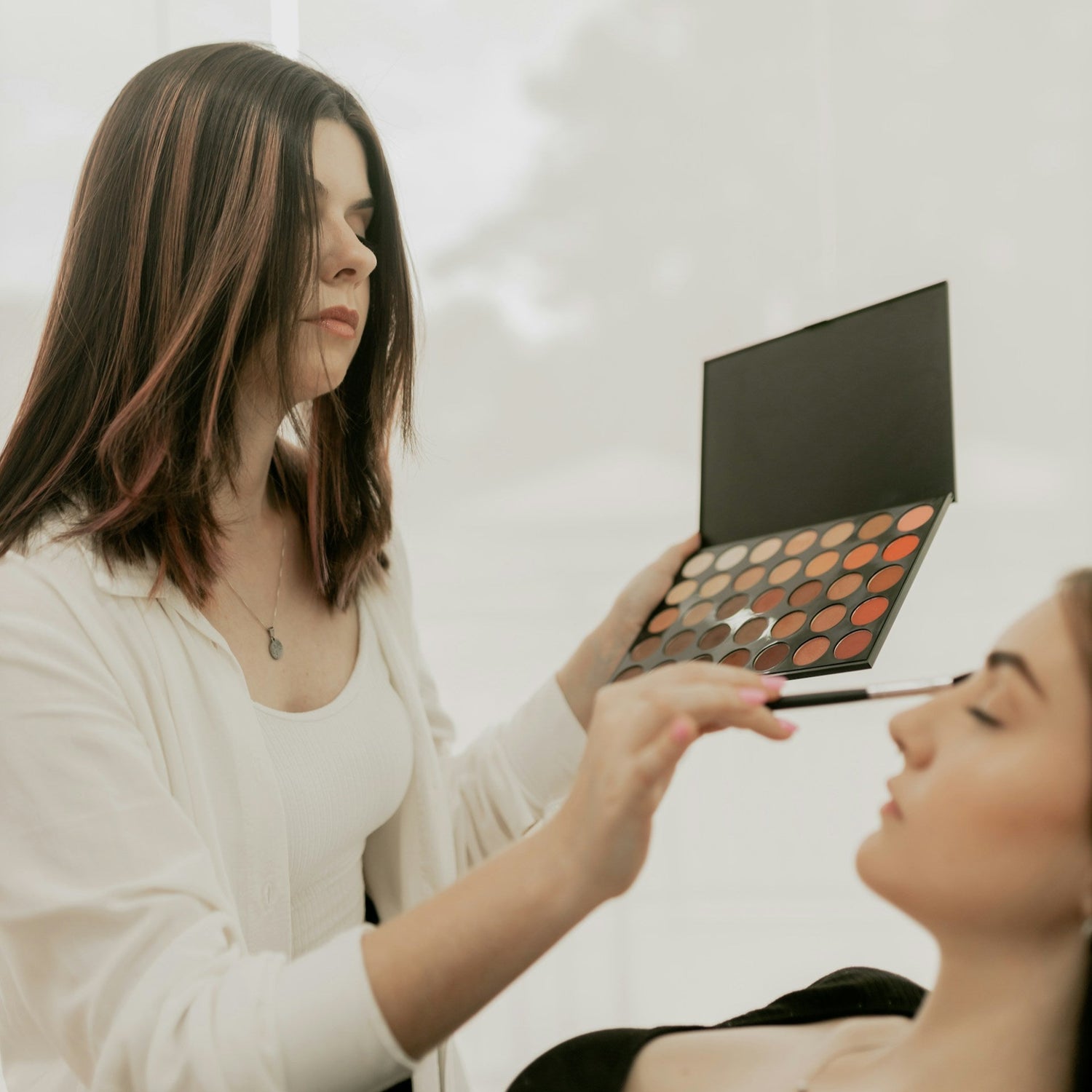 Beauty artist holding a palette and doing makeup for a client