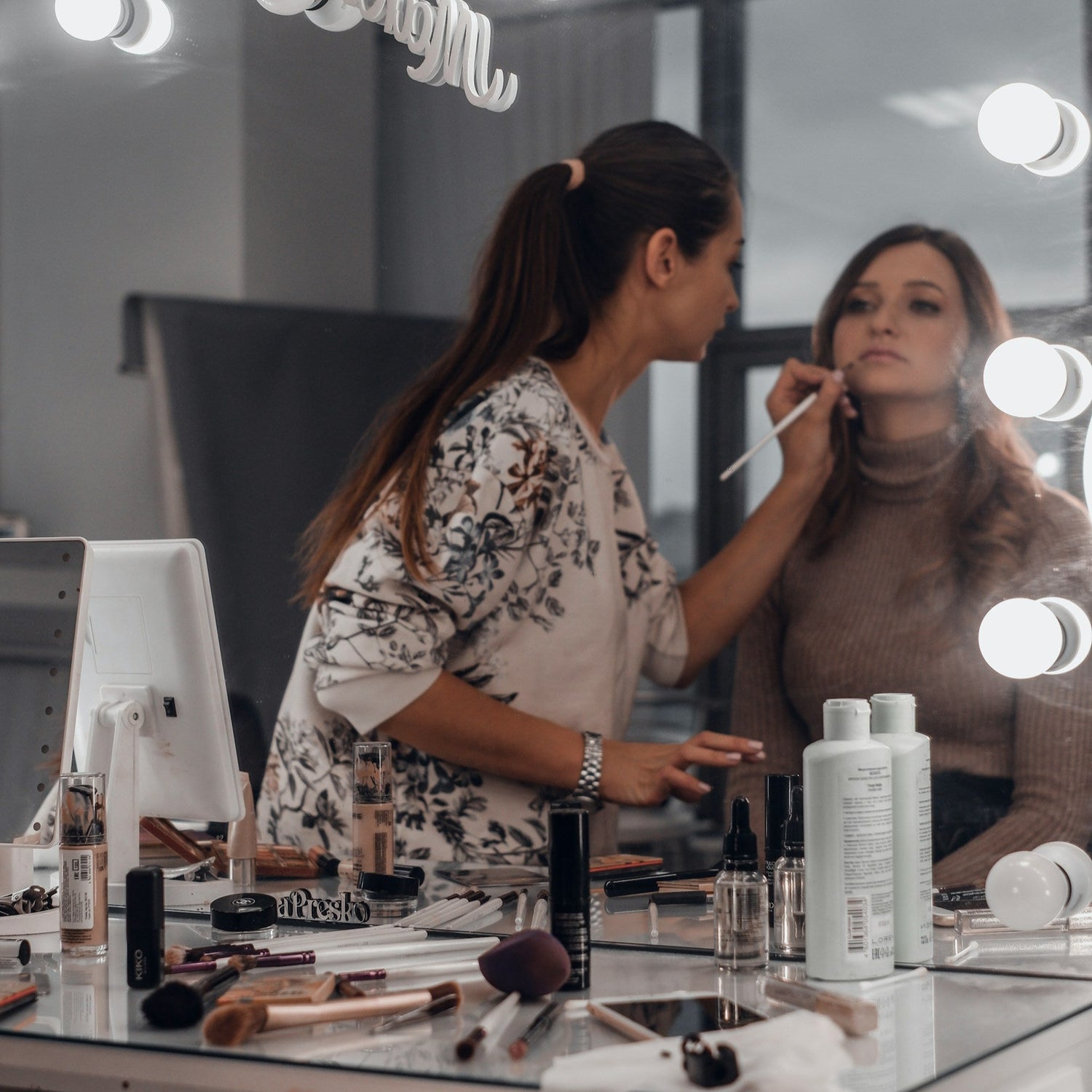Makeup artist working on a client in front of a well-lit mirror