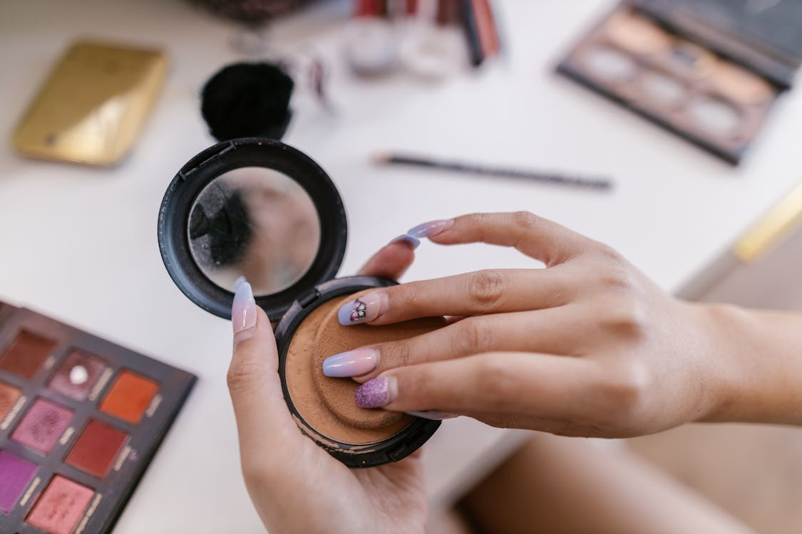 Person holding a powder puff with makeup palettes on white surface